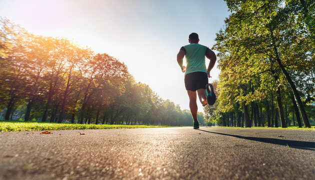 A runner man running alone toward the sun in the park with tree on both side of the road.
