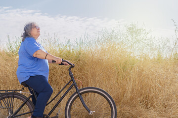 Naklejka premium an older woman with white hair, obese, seen in profile riding a bicycle along a sunlit, overgrown pathway