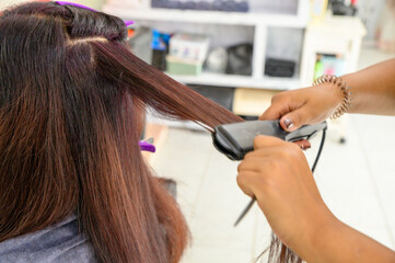 Fototapeta premium A beautician is straightening the hair of a female customer to make it straight at a beauty salon in Thailand.