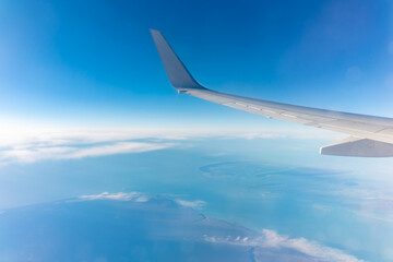 View from the airplane window at a beautiful blue clear sky, earth, sea and the airplane wing