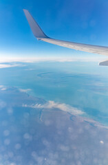Obraz premium View from the airplane window at a beautiful blue clear sky, earth, sea and the airplane wing