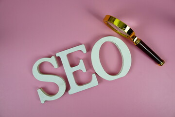 Seo words (Search Engine Optimization) letters with magnifying glass on pink background