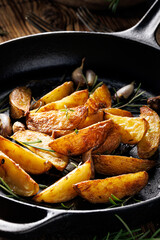 Baked potato wedges seasoned with rosemary and garlic on a black cast iron pan, close-up