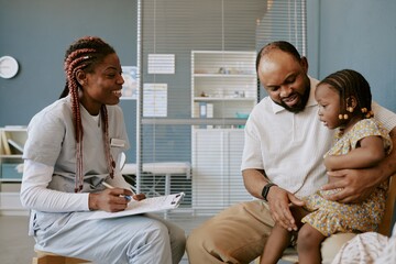Nurse wearing scrubs speaking with father holding young child in modern clinic setting Perfect...