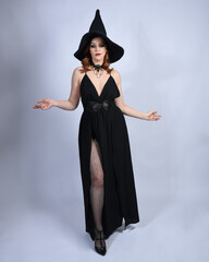 Full length portrait of beautiful female red head model wearing  glamorous black witch dress with...