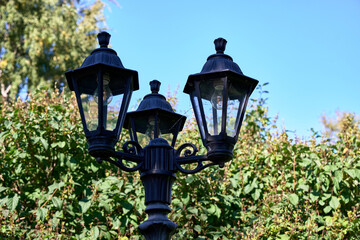 Three black street lamps are lit up in the daytime