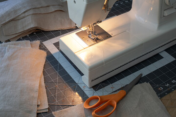 Close view of a sewing machine, orange scissors, ruler and pieces of linen fabric.