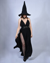 Full length portrait of beautiful female red head model wearing  glamorous black witch dress with...