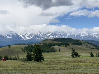 Mountains and meadows in cloudy weather. Snow-covered mountain tops.