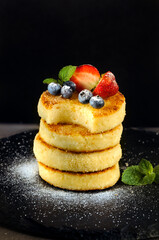 Fresh cheesecakes decorated with blueberries and strawberries with mint, sprinkled with powdered sugar on a black background. Vertical image with copy space