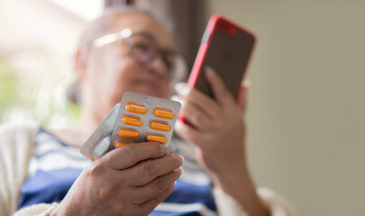 Senior woman holding medicine pills using digital tablet to make video conference call to doctor