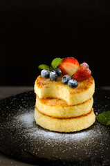 Fried cheesecakes with different berries blueberries and strawberries on a dark background. Vertical image with space for text