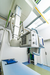 Modern X-ray machine in a bright medical facility. A cutting-edge X-ray machine hangs from the ceiling in a well-lit medical room, ready for diagnostic imaging procedures.