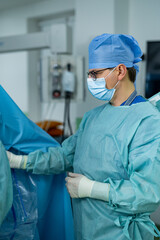 Surgeon in sterile surgical attire. A surgeon in scrubs uses sterile techniques while assisting in...