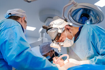 Surgeons in a high-tech operating room. Two surgeons in blue scrubs and masks focus intently on a...