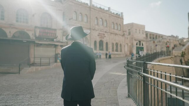 Sunlight on an Orthodox Jew walking beside bars on a steep slope in the Old City of Jerusalem, Israel