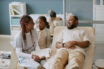 Fototapeta premium Medical professional consulting and discussing health concerns with patient and child in modern clinic setting. Clinic backdrop including medical equipment and documents