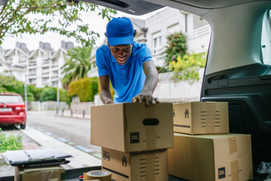 Smiling delivery man arranging packages in the trunk of his car.