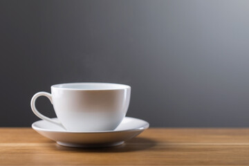 White coffee cup sits on a wooden table against a dark gray background. The image conveys warmth, simplicity, and the comfort of enjoying a fresh cup of coffee