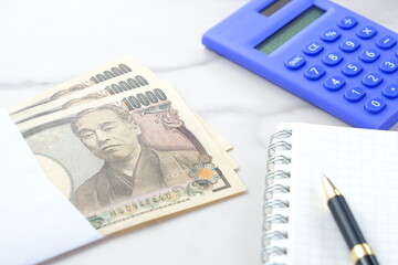 福沢諭吉の肖像の一万円紙幣と電卓、メモ帳とペン
