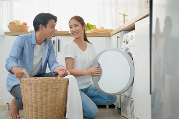 Happy young asian couple doing laundry fold clothes together using a front loading washing machine...