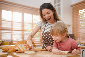 Mother and son preparing the dough, bake a bakery for breakfast in the morning. Cute child helping her beautiful caring parent. Happy family in the kitchen.