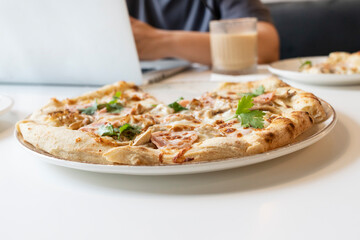 Close-up photo of delicious pizza and man working on laptop on the background in the cafe	
