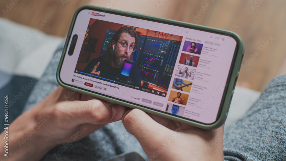 Poster caucasian boy watches educational video of blogger about stock trading using mobile phone while sitt