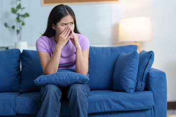 Obraz premium A woman with a sneeze is feeling unwell. Runny nose and sneezing, stomach ache, sore throat, fatigue in the living room on the sofa in the house. Feeling bad and having allergies treatment concept.
