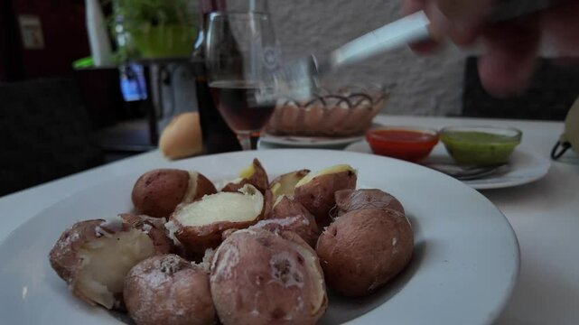 Closeup view of the hand of a man eating papas con mojo pic&oacute;n, traditional Canarian food seated outdoor.