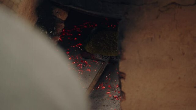 Placing 2 baking trays with paraguayan soup, into the tatakua with coals. The tatakua is a traditional Paraguayan clay oven. Paraguayan soup is the only solid soup in the world