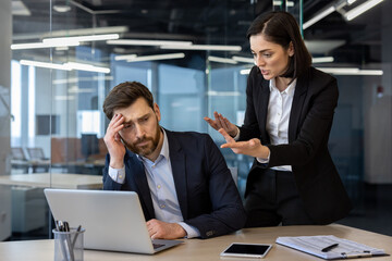 Conflicted office scene showing an angry female boss yelling at a frustrated male employee working on laptop. Tension highlights workplace stress and pressure during a business meeting.