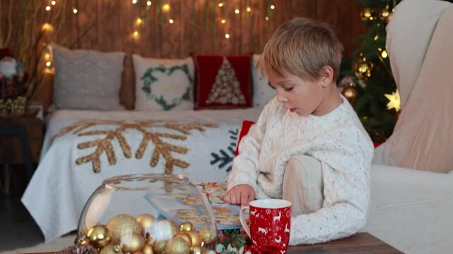 Cute blond child, boy, celebrating Christmas at home, decorated room for the holidays, child reading book and playing