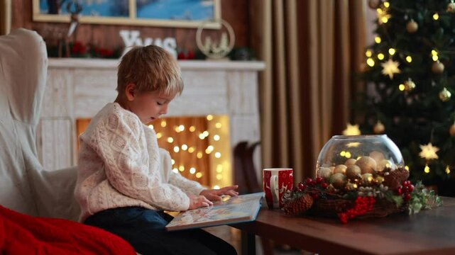 Cute blond child, boy, celebrating Christmas at home, decorated room for the holidays, child reading book and playing