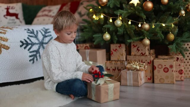 Cute blond child, boy, celebrating Christmas at home, decorated room for the holidays, child reading book and playing