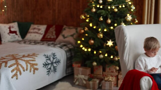 Cute blond child, boy, celebrating Christmas at home, decorated room for the holidays, child reading book and playing