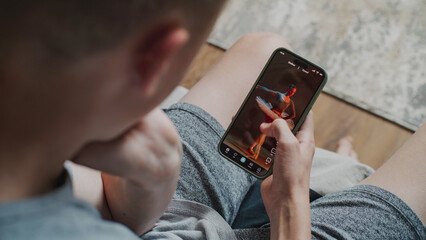 Teen boy scrolls through and watches social network feed with short videos using mobile phone while...