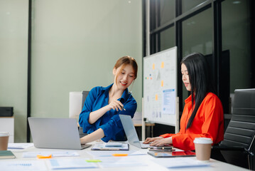 ￼￼Two young Asian professionals engaged in teamwork and business discussions in modern office