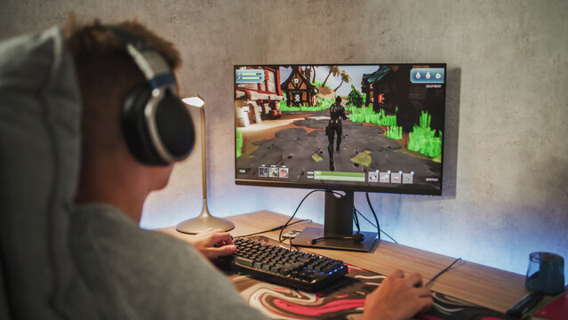 Caucasian teenager wearing headphones plays online video game on PC, spends leisure time at home. Professional young gamer enjoys gameplay in 3D third person shooter on computer. Gaming and Esports.
