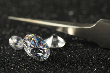 Beautiful dazzling diamonds and tweezers on dark shiny background, closeup