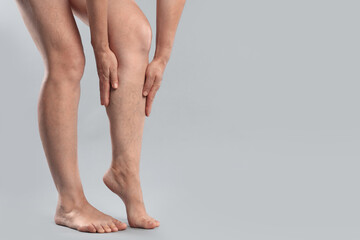 Woman suffering from varicose veins on grey background, closeup. Space for text