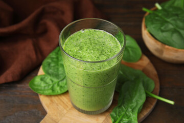 Tasty green smoothie in glass and spinach on wooden table, closeup
