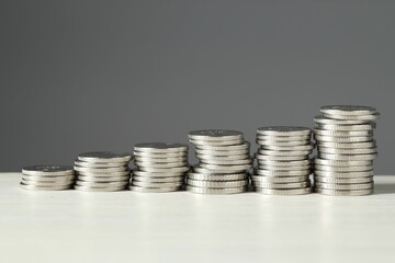Stacked coins on white wooden table against grey background, closeup. Salary concept