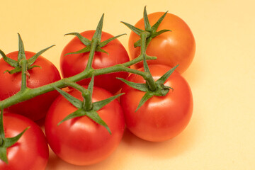 Red cherry tomatoes with green branch on yellow background