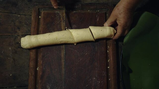A overhead shot of a woman cutting Paraguayan chipa to put in the oven and baked in a tatakua, a traditional Paraguayan clay oven.