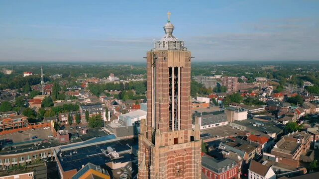 Drone footage of Sint Martinus Kerk's tower in Weert, showcasing the clock, spire, and cross against the backdrop of the Limburg town and surrounding landscape. Location: Weert, Nederland