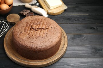Tasty chocolate sponge cake and ingredients on black wooden table