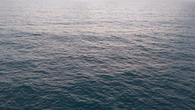 Slow-motion drone shot over ocean waves at sunrise. Colors of blue and orange fill the sky as clouds rise on the horizon. Various angles capture the sea&rsquo;s movement.