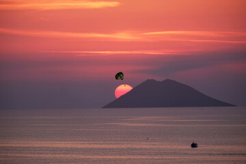Stromboli volcano island profile with sun in the background.