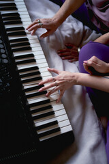 Fototapeta premium A 60-year-old mother and a 40-year-old daughter play the keyboard together on the bed at home